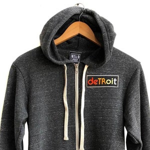 May include: A dark gray hooded sweatshirt with a zipper closure and a colorful "deTRoiT" patch on the front.