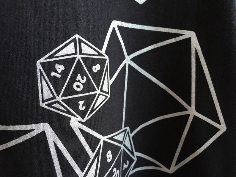 May include: Black fabric with a silver geometric design featuring multiple polyhedral dice. The dice are numbered, with the largest die showing the number 20. The design is a repeating pattern.
