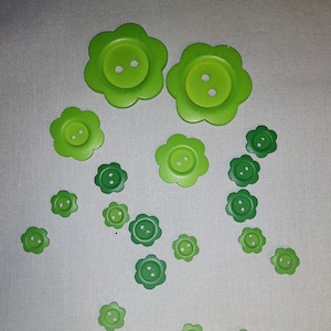 May include: A collection of green flower-shaped buttons of various sizes. The buttons have a light green center and a darker green outer edge.