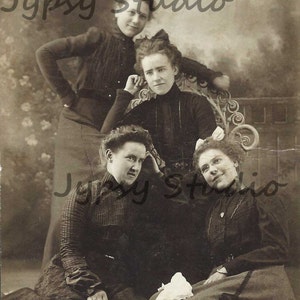 Puede incluir: Una fotografía vintage en blanco y negro de cuatro mujeres con vestidos posando para un retrato. Las mujeres están sentadas y de pie frente a un fondo con el texto "Jypssy Studio" escrito en la parte superior.
