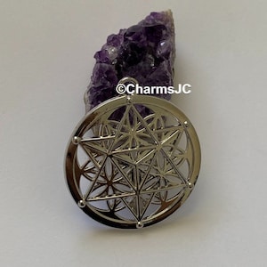 May include: Silver pendant featuring a geometric design with a star in the centre. The pendant is on a purple amethyst crystal.
