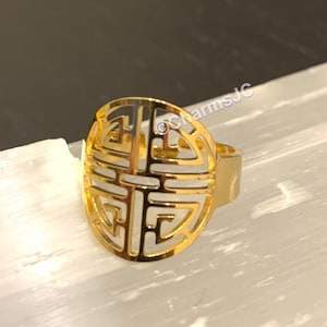 Può includere: Anello in oro con un designo a taglio di un simbolo cinese. Il simbolo è un cerchio con un quadrato all'interno, e il quadrato ha quattro quadrati più piccoli all'interno.