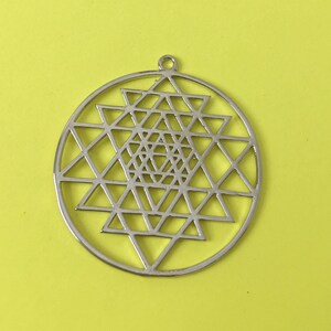 May include: A silver pendant featuring a Sri Yantra design, a geometric symbol representing the universe.