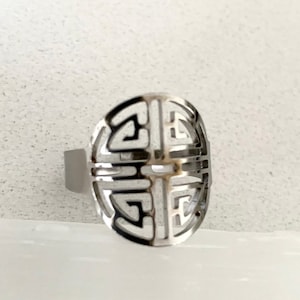 Può includere: Un anello d'argento con un design geometrico. L'anello è in metallo e ha una forma circolare.