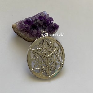 May include: Silver pendant featuring a geometric design with a star in the centre. The pendant is on a white background with a purple amethyst crystal cluster.