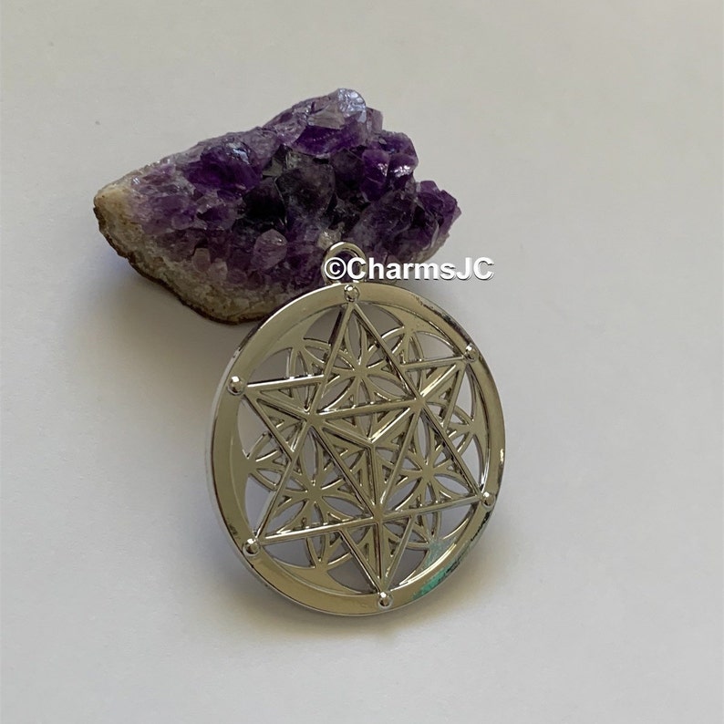 May include: Silver pendant featuring a geometric design with a star in the centre. The pendant is on a white background with a purple amethyst crystal cluster.