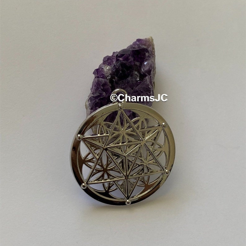 May include: Silver pendant featuring a geometric design with a star in the centre. The pendant is on a purple amethyst crystal.