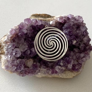 May include: Silver pendant with a spiral design, set against a background of amethyst crystals.