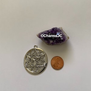 May include: Silver pendant featuring a geometric design with a star in the centre. The pendant is about the size of a UK penny.