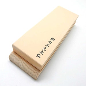 Peut inclure: Une pierre à aiguiser rectangulaire de couleur brun clair avec une base en bois. La pierre porte une inscription japonaise qui se traduit par "pierre à aiguiser naturelle".