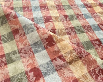 May include: Close-up of a woven fabric with a plaid pattern. The fabric features a mix of colors including red, yellow, green, and blue. Floral designs are woven into the fabric, adding texture and detail. The fabric is folded, showing its texture.