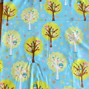 May include: A blue fabric with a repeating pattern of green trees with owls and colorful flowers. The owls are in various colors, including pink, blue, and green.