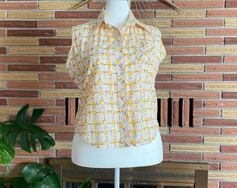 Pode incluir: Uma camisa sem mangas com botões, apresentando um padrão repetitivo de quadrados amarelos e brancos, âncoras e lemes de navio. A camisa tem uma gola pontiaguda e uma carcela frontal, exibida num torso de manequim branco.