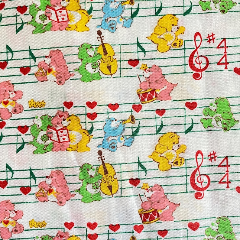 May include: White fabric with a repeating pattern of colorful cartoon bears playing musical instruments. The bears are pink, yellow, green, and blue. Musical notes, red hearts, and musical symbols are also present.