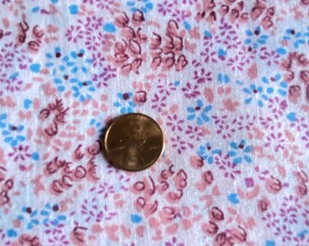 May include: White fabric with a pink and blue floral pattern. The fabric is textured and has a subtle sheen. A penny is placed on the fabric for scale.