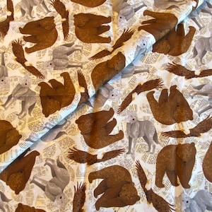 May include: Fabric with a repeating pattern of brown bears, gray wolves, and brown eagles on a cream-colored background with a newspaper print design. The fabric is folded, showing the pattern's repeating nature.