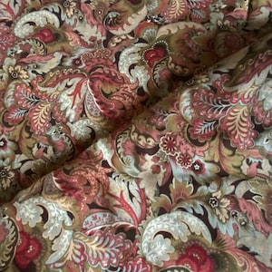 May include: Close-up of a fabric with a detailed paisley pattern. The design features swirling floral and leaf motifs in shades of red, brown, green, and blue on a dark background. The fabric has a soft, textured appearance.