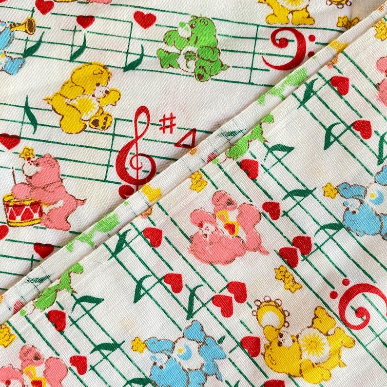 May include: White fabric with a repeating pattern of colorful cartoon bears, musical notes, red hearts, and musical symbols. The bears are in various poses, some playing instruments. The musical notes are green, and the musical symbols are red.