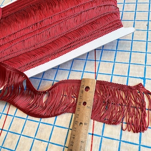 May include: Red fringe trim with a length of 30 inches. The fringe is made of a soft, woven fabric and has a subtle sheen.