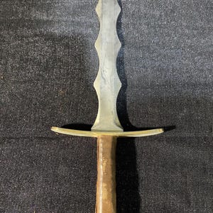 May include: A medieval-style sword with a silver-colored blade and a brown leather-wrapped handle. The sword features a crossguard and a pointed tip. The blade has a series of decorative indentations along its length.