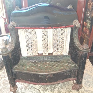 May include: An antique black and white chair with ornate details. The chair has a curved back, decorative armrests, and a patterned seat. The back has a red accent, and the seat has a diamond pattern.