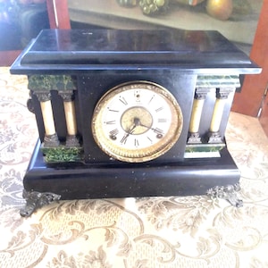 May include: A black marble mantle clock with gold accents and a white face. The clock has Roman numerals and a green marble trim.