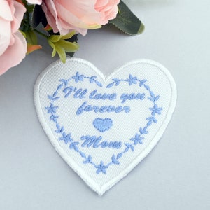 May include: White heart-shaped patch with blue embroidery that reads "I'll love you forever Mom" surrounded by a blue floral design.
