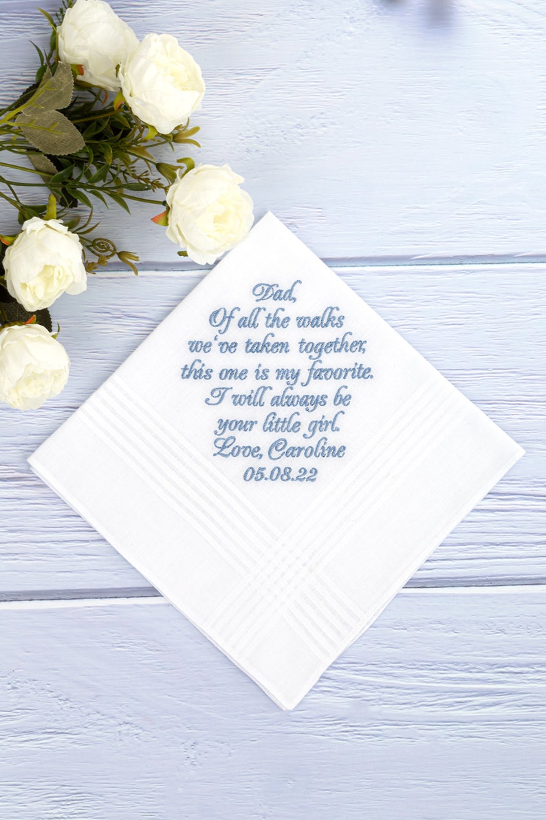 May include: White handkerchief with blue embroidered text that reads: "Dad, Of all the walks we've taken together, this one is my favorite. I will always be your little girl. Love, Caroline 05.08.22"