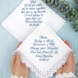 May include: Two white handkerchiefs with lace trim and blue embroidered messages for a bride's father and mother. The father's handkerchief reads "Dad, Of all the walks we've taken together, this one is my favorite. I will always be your little girl. Love, Caroline 05.08.22". The mother's handkerchief reads "Mom, Today a Bride Tomorrow a Wife Always your Daughter And best friend for life. Love, Caroline 05.08.22".