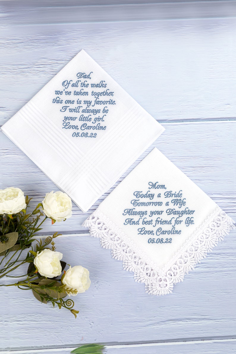 May include: Two white handkerchiefs with blue embroidered text. The top handkerchief has the text "Dad, Of all the walks we've taken together, this one is my favorite. I will always be your little girl. Love, Caroline 05.08.22". The bottom handkerchief has the text "Mom, Today a Bride Tomorrow a Wife Always your Daughter And best friend for life. Love, Caroline 05.08.22".