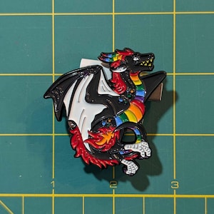 May include: A black and white enamel pin of a rainbow dragon with red, orange, yellow, green, blue, indigo, and violet scales. The dragon has a black body with white wings and a red head. The dragon is in a curled position with its wings spread out.