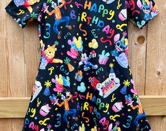 Può includere: Abito nero con scollo tondo con un tema di compleanno colorato. L'abito presenta personaggi dei cartoni animati, palloncini, regali, cupcake e le parole "Happy Birthday". L'abito è a maniche corte e ha una gonna svasata.