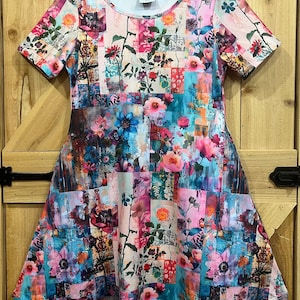 Puede incluir: Vestido de manga corta con un colorido diseño de patchwork floral. El vestido presenta un escote redondo y una falda acampanada. La tela es una mezcla de tonos rosas, azules y verdes, con el texto "Ellie Liggins" visible en el escote.