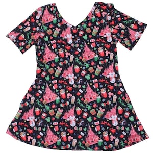 May include: A black short-sleeved dress with a festive Christmas print featuring the iconic Cinderella's Castle, Mickey Mouse, and other Disney characters. The print also includes holiday elements like snowmen, candy canes, and mugs of hot chocolate.