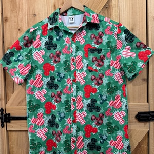 Op de afbeelding: Groen, kort mouwig overhemd met knopen en een kerstthema print met Mickey Mouse-koppen, sneeuwvlokken en snoepstokken.