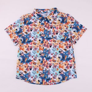 May include: A white short-sleeved button-down shirt with a colourful all-over print of Mickey Mouse and Minnie Mouse dressed as sailors. The print also includes anchors, seashells, and nautical flags.