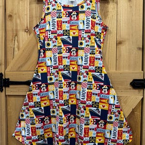 May include: A sleeveless A-line dress featuring a colourful nautical-themed grid pattern. The print includes Mickey and Minnie Mouse, cruise ships, anchors, life preservers, and telescopes, with text reading AHOY, CRUISE, and SET SAIL in red, blue, and yellow.