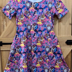 May include: A pink and blue short-sleeved dress with a print of Belle and the Beast from Beauty and the Beast. The print features roses, hearts, and clocks.