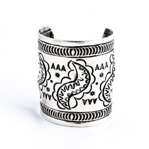 May include: A silver cuff bracelet with a paisley design. The bracelet is decorated with a repeating pattern of stylized paisley shapes and a border of small circles.