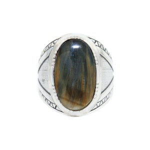 May include: A silver ring featuring an oval blue and brown tiger's eye gemstone set in a silver bezel. The ring band has a decorative design of triangles.