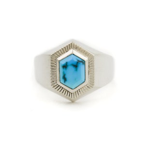 May include: A silver ring with a turquoise gemstone set in a hexagonal bezel. The ring has a textured band and a polished finish.