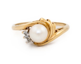 May include: A gold ring with a white pearl and small diamonds. The ring has a swirl design.