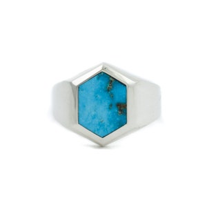 May include: A silver ring with a turquoise gemstone set in a hexagonal shape.