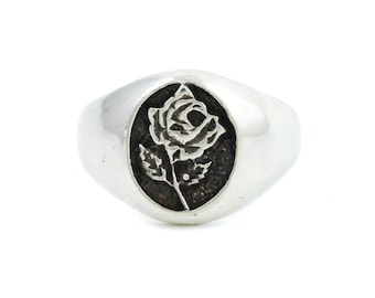 May include: A silver signet ring with a black rose design.