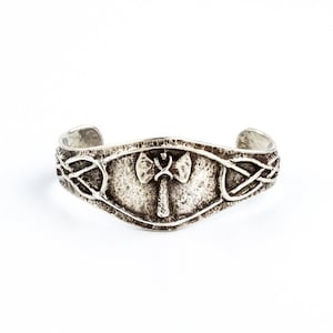 以下が含まれることがあります： 中央に斧の浮き彫りがある、ケルトの結び目のデザインのシルバーブレスレットです。