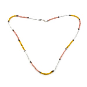 Può includere: Una collana fatta di piccole perline colorate in giallo, rosa e bianco. Le perline sono infilate su una catena d'argento.
