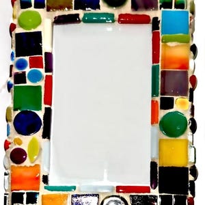 Op de afbeelding: Een rechthoekig mozaïek spiegel frame met een witte binnenkant. Het frame is versierd met kleurrijke glazen tegels in verschillende vormen, waaronder vierkanten, rechthoeken en cirkels. De tegels zijn in tinten blauw, groen, rood, oranje en geel.