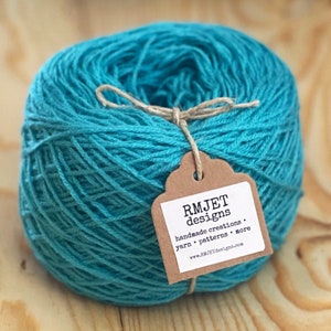 May include: A skein of teal blue yarn with a brown tag that reads "RMJET designs. handmade creations. yarn. patterns. more www.RMJETdesigns.com"