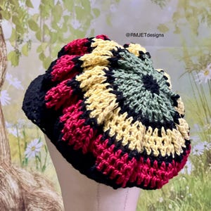 May include: A handmade crochet hat in a vibrant color scheme. The hat features a black base with sections of red, yellow, green, and black crochet stitches. The text "@RMJETdesigns" is visible on the image.