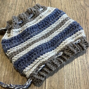 May include: A striped crocheted hat in shades of brown, white, and blue. The hat is made with a thick yarn and has a textured, hand-knitted look.